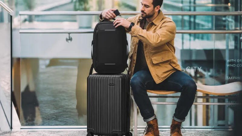 Viajero con mochila Nomatic sobre una maleta